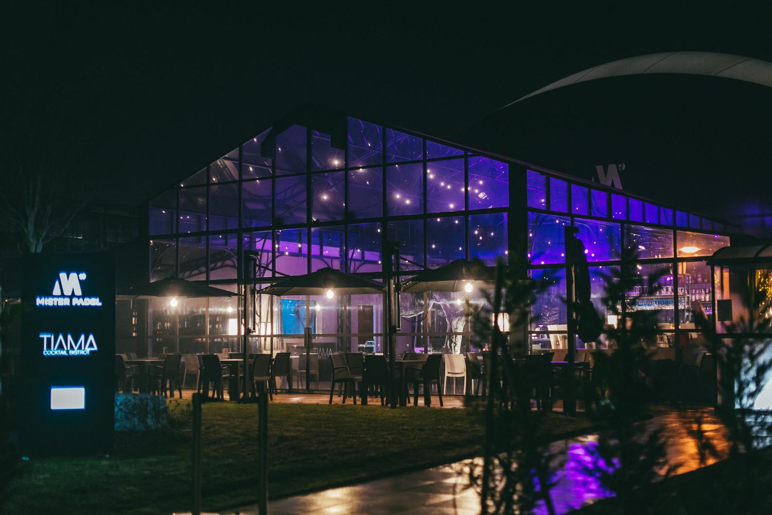 La club house TiAma di sera, con la vetrata illuminata e l'insegna Mister Padel